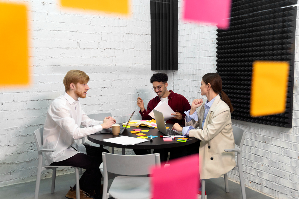 Equipe de comunicação reunida em uma sala de reuniões, discutindo ideias criativas para uma ação de PR, com anotações, notebook e quadros de brainstorming ao fundo.